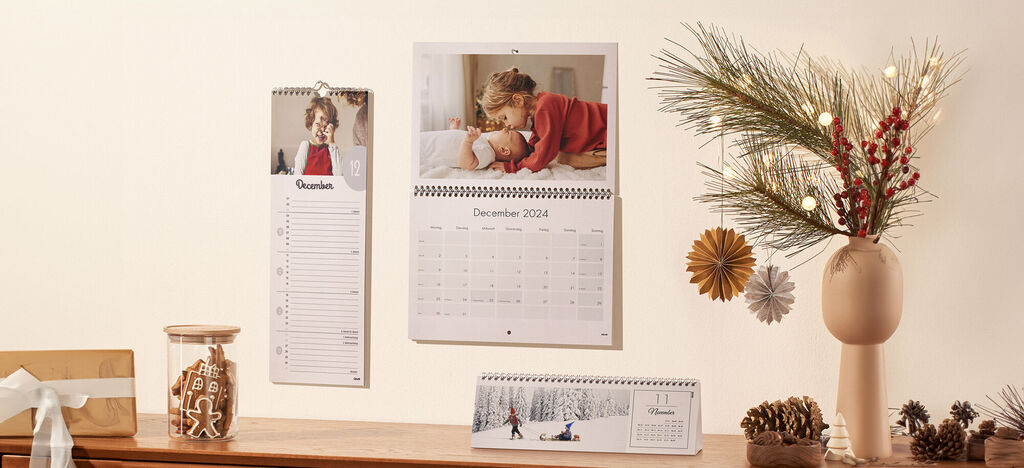 Een adventkalender en een wandkalender met familiefoto's hangen aan een muur met dennentakken en decoratie.