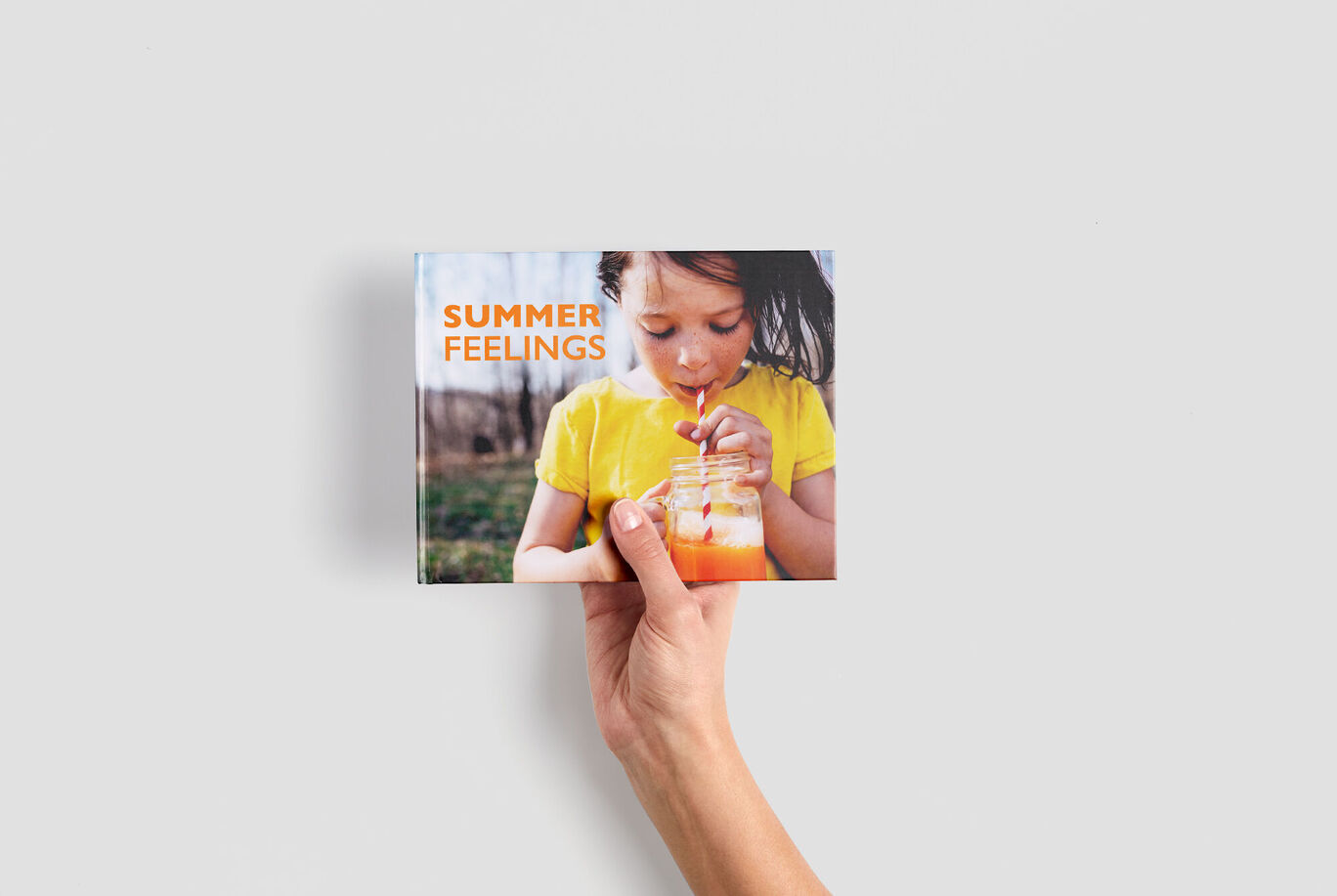 Een hand houdt een CEWE Fotoboek vast met de titel "Summer Feelings".